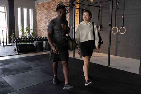 Diverse friends walking and talking in warehouse gym carrying gym bags and water bottles