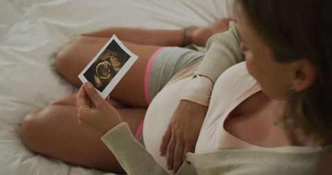 Expectant mother viewing ultrasound photo on bed