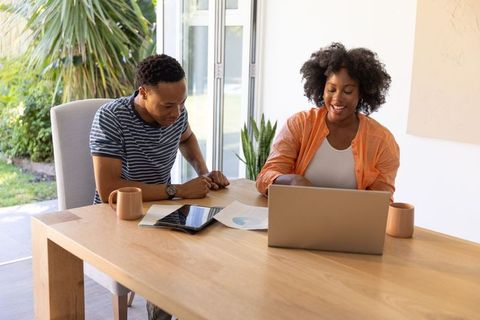 Young couple collaborating on home finances using laptop and tablet at dining table