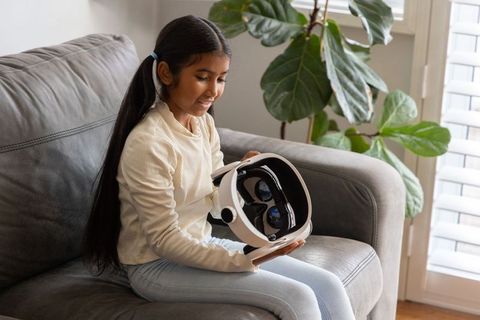 Indian girl holding white vr headset on grey sofa exploring virtual reality imagination