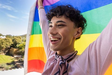 Cheerful young person celebrating pride on balcony with rainbow flag