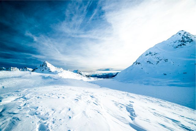 Majestic snow-covered mountains under a dramatic blue sky. Perfect for use in travel brochures, outdoor adventure advertisements, and holiday destination guides. Ideal for conveying themes of tranquility, nature’s grandeur, and the beauty of cold, remote locations.