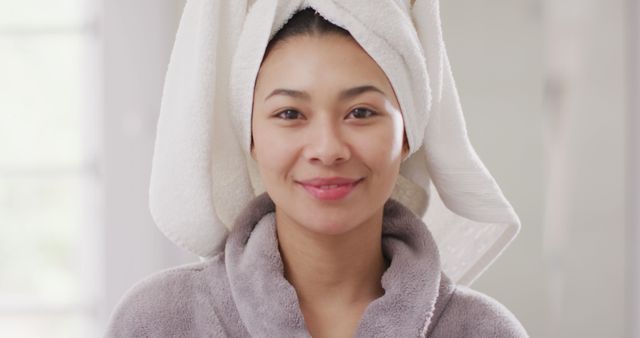 Image of portrait of smiling biracial woman with towel on hair in bathroom. Health and beauty, leisure time, domestic life and lifestyle concept.