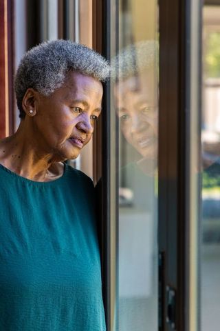 Senior african woman gazing through glass door, reflecting on memories and resilience
