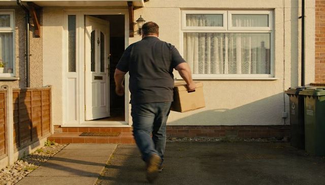Courier walking toward house carrying cardboard box on suburban driveway