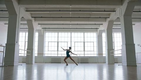 Contemporary ballet dancer practicing solo in bright industrial loft studio with barre