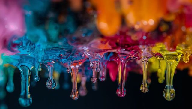 Vibrant colorful paint droplets dripping in macro with glossy reflections and bokeh
