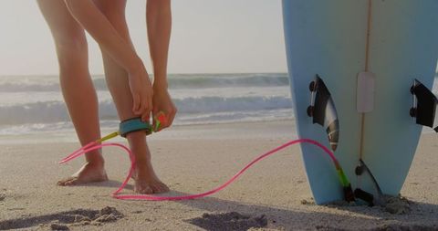 Surfer tying leash to surfboard on sandy beach