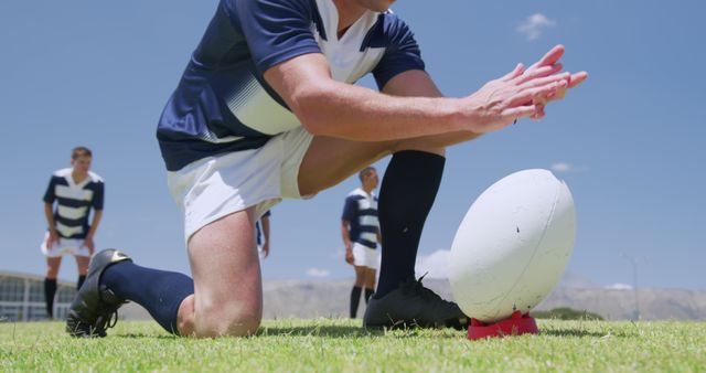 Low section of caucasian male rugby player positioning ball on tee to kick on sunny sports field. Preparation, sport, team sport and competition, unaltered.