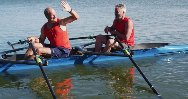 Two senior caucasian men in rowing boat high fiving. sport retirement leisure hobbies rowing healthy outdoor lifestyle.