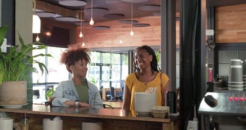 African american women chatting and smiling behind wooden counter in modern coffeehouse