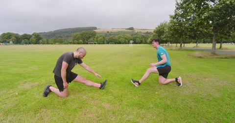Two Men Stretching on Grass Preparing for Outdoor Workout