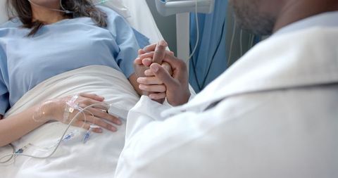 Caring male doctor consoling female patient in hospital bed