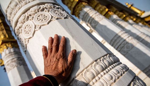 Senior pilgrim touching carved marble column at temple with gilded capitals