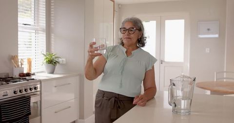 Elderly Woman Enjoying Hydration Moment in Bright Modern Kitchen