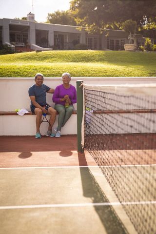 Smiling Senior Couple Relaxing on Tennis Court Bench