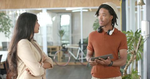 Multicultural Coworkers Collaborating in Modern Open Office Holding Tablet and Headphones