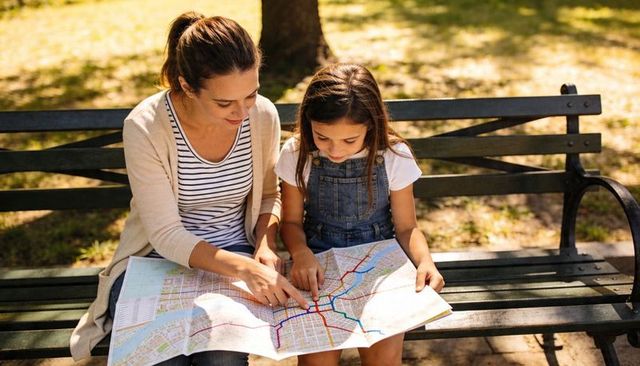 Mother and daughter studying city map on park bench, planning urban adventure together