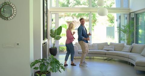 Young couple dancing playfully in bright modern living room with curved sectional sofa