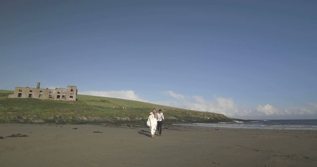 Couple Walking on Beach Near Old Stone Building Under Clear Blue Sky - Download Free Stock Images Pikwizard.com