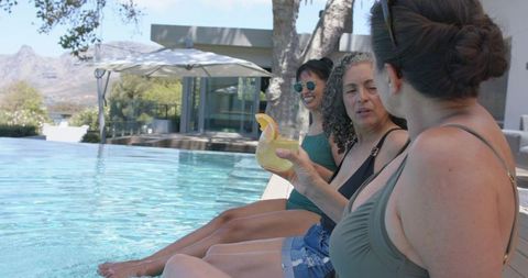 Three friends lounging poolside sharing cocktail on sunny modern patio