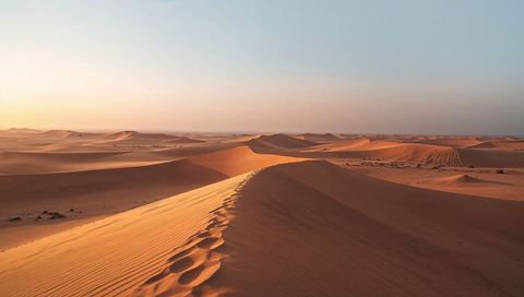 Sunlit sand dune ridge curving across desert with footprints and wind ripples at sunrise