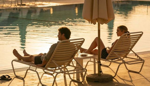 Couple relaxing on poolside loungers at golden sunset with swimwear, drink and flip-flops