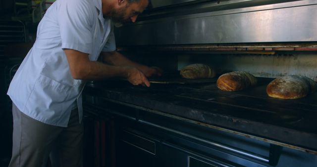 Baker taking fresh bread loaves out of industrial oven in bakery - Download Free Stock Images Pikwizard.com