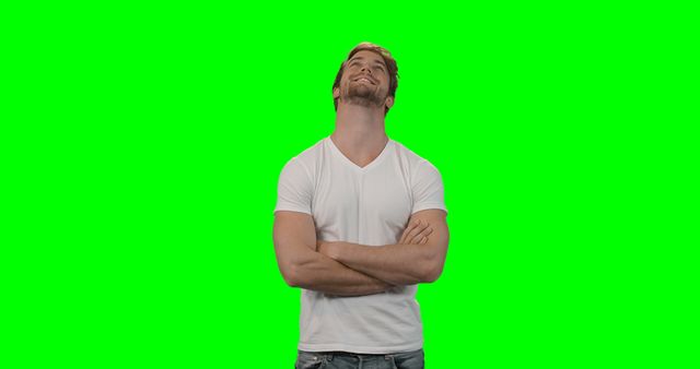 Man standing with arms crossed, smiling and looking up against green chroma key background. Suitable for video editing, compositing, presentations, and advertisements.