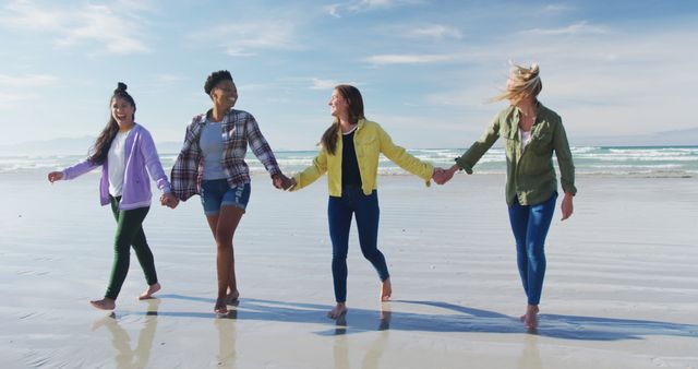 Happy group of diverse female friends having fun, walking along beach holding hands. holiday, freedom and leisure time outdoors.