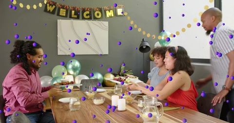 Friends Passing Dishes at Casual Welcome Dinner Party with Balloons, Candles and Banner