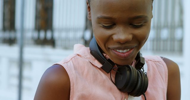 Young woman wearing headphones and smiling while outdoors. Perfect for use in lifestyle blogs, advertisements for music and audio products, or articles focusing on happiness and leisure activities.