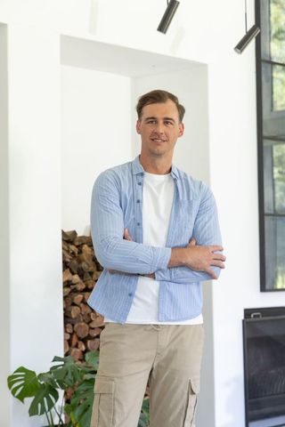 Confident man standing in modern living room with stacked firewood and monstera