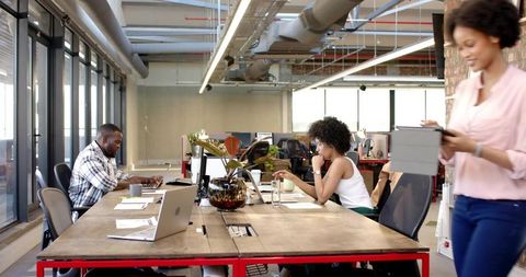 Open-plan team collaborating at long shared desk using laptops and tablet in modern workspace