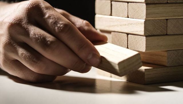 Adult hand pulling wooden block from stacked tower conveying tension and strategy