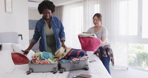 Diverse Couple Joyfully Packing Suitcases in Bright Bedroom