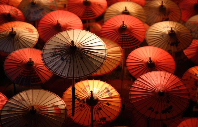 This image features a collection of traditional paper umbrellas illuminated by vibrant lighting, showcasing the intricate craftsmanship. Suitable for use in travel blogs, articles on Asian markets, cultural presentations, and designs needing colorful, traditional elements.