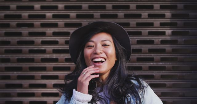 Portrait of happy asian woman wearing hat, laughing in city street. City living and modern urban lifestyle.
