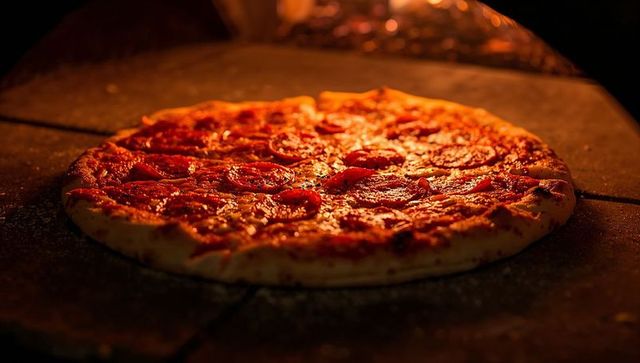 Baking pepperoni pizza on stone oven floor, bubbling cheese and crispy cornmeal crust