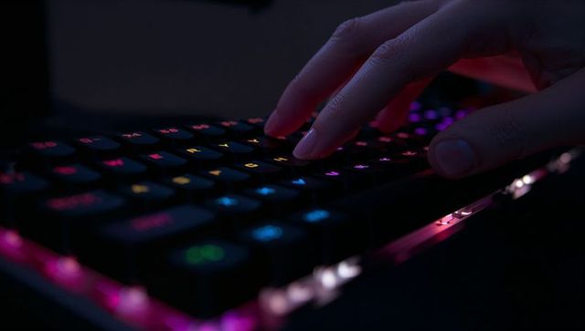 Close-up gamer hand typing on rgb mechanical keyboard with neon backlight glow