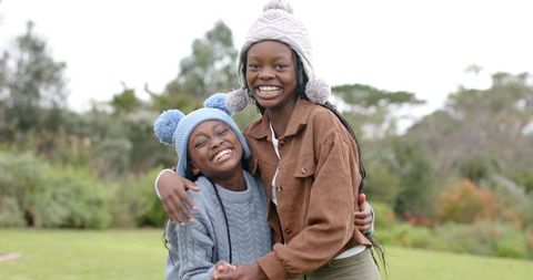 African American sisters laughing and hugging outdoors wearing pom-pom hats and knit sweaters