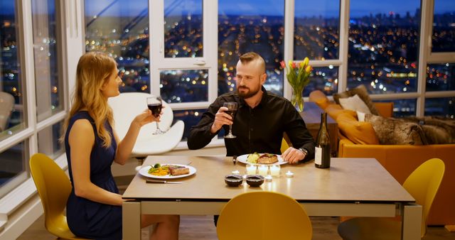 A Caucasian couple enjoys a romantic dinner with a cityscape view at night, with copy space. Their intimate setting with wine and a well-set table creates an ambiance of elegance and connection.