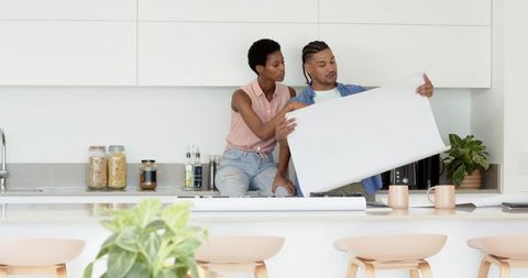 Diverse Couple Reviewing Blueprint on Modern Kitchen Counter Island
