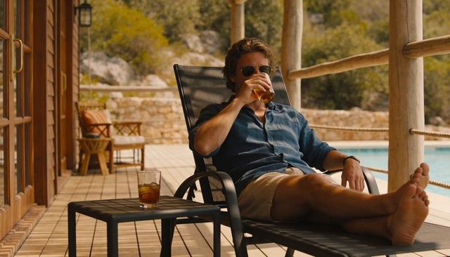 Relaxing man drinking iced beverage on poolside lounge chair during sunny villa vacation