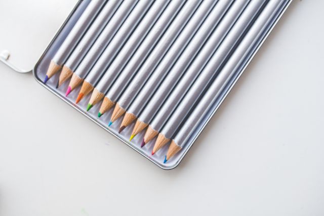 Tin box with neatly arranged colored pencils on white background. Ideal for art related projects, educational materials, creativity concepts, and back-to-school campaigns.