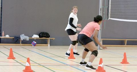 Diverse female volleyball teammates practicing cone agility drill on indoor court