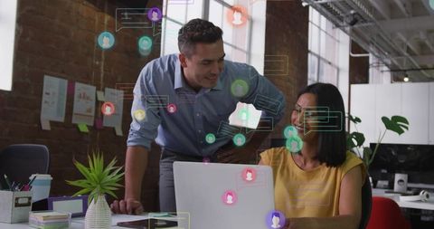 Colleagues collaborating around laptop with digital chat overlays in modern industrial office