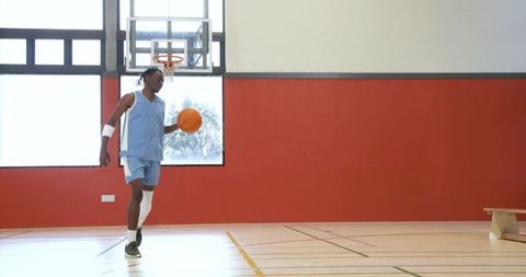 Athlete dribbling basketball on indoor court with red wall