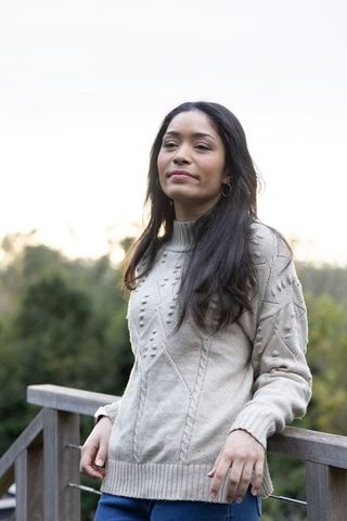 Young woman leaning on deck railing, gazing into distance, wearing knit sweater and jeans