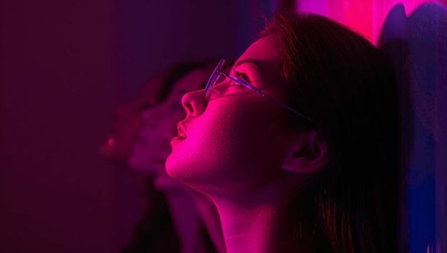 Introspective Woman with Glasses in Moody Neon Light